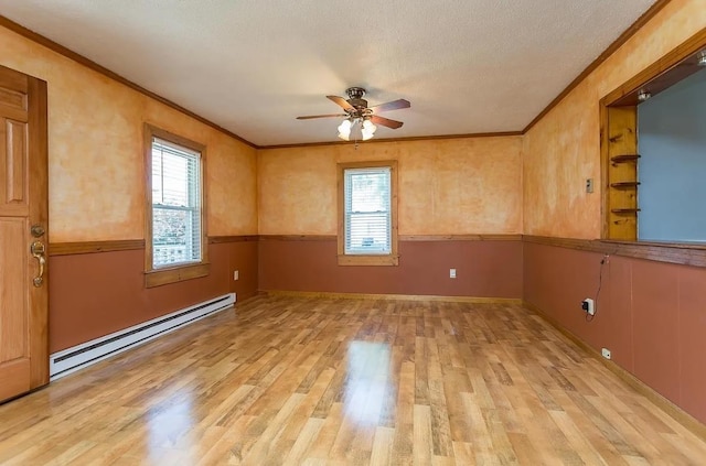 empty room with a healthy amount of sunlight, ornamental molding, a baseboard heating unit, and light wood-type flooring