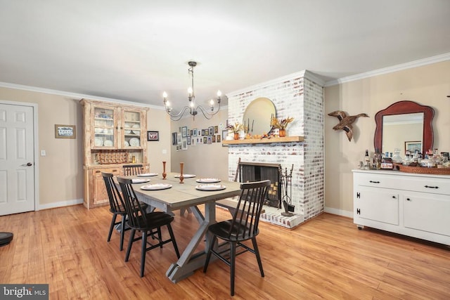 dining space featuring a chandelier, a brick fireplace, crown molding, and light wood-style floors