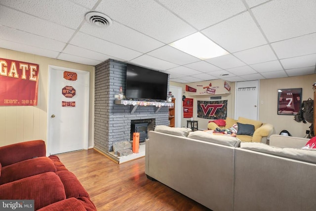 living room with visible vents, a drop ceiling, a brick fireplace, and wood finished floors