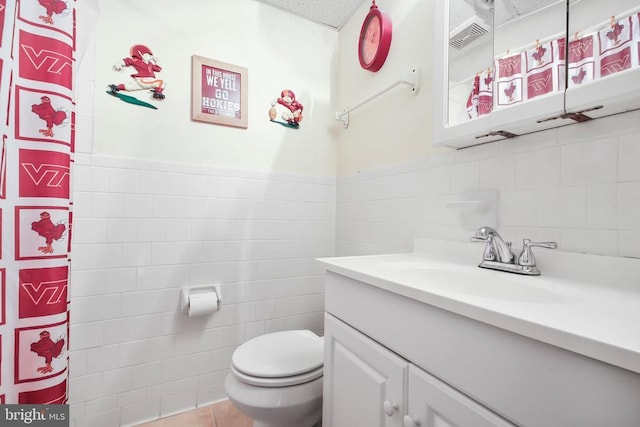 bathroom with vanity, a wainscoted wall, tile walls, toilet, and tile patterned floors