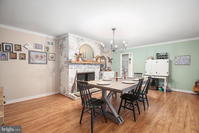 dining space with visible vents, ornamental molding, light wood-style flooring, a fireplace, and a notable chandelier