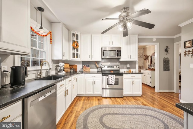 kitchen featuring dark countertops, ornamental molding, white cabinets, stainless steel appliances, and a sink