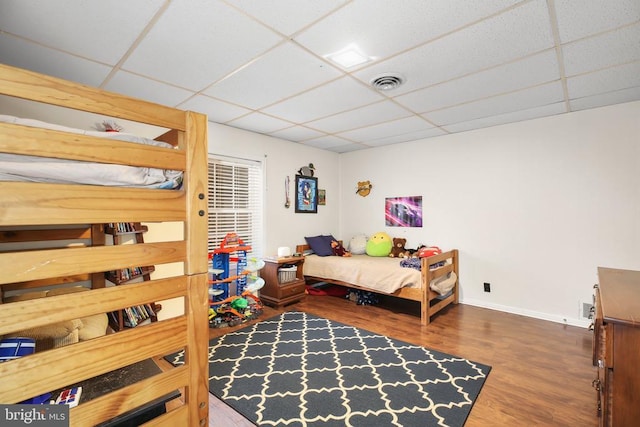 bedroom featuring visible vents, a paneled ceiling, baseboards, and wood finished floors