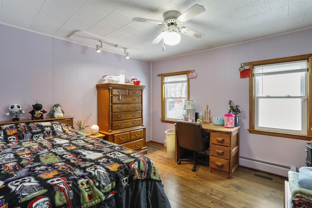 bedroom with rail lighting, visible vents, baseboard heating, a ceiling fan, and light wood-type flooring