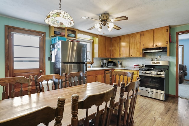 kitchen with light countertops, appliances with stainless steel finishes, light wood-style floors, a sink, and under cabinet range hood