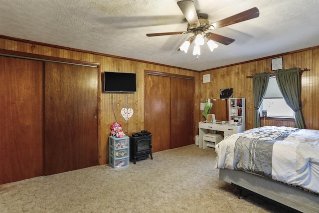 carpeted bedroom with ornamental molding, a wood stove, a textured ceiling, wood walls, and two closets