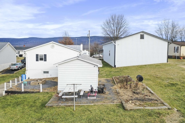 back of property with a yard, a vegetable garden, an outdoor structure, and a mountain view