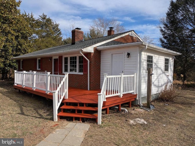 back of house with a wooden deck, brick siding, roof with shingles, and a chimney