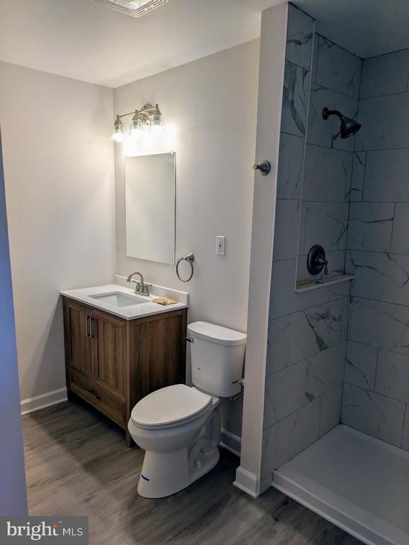 bathroom featuring vanity, toilet, wood finished floors, and a tile shower