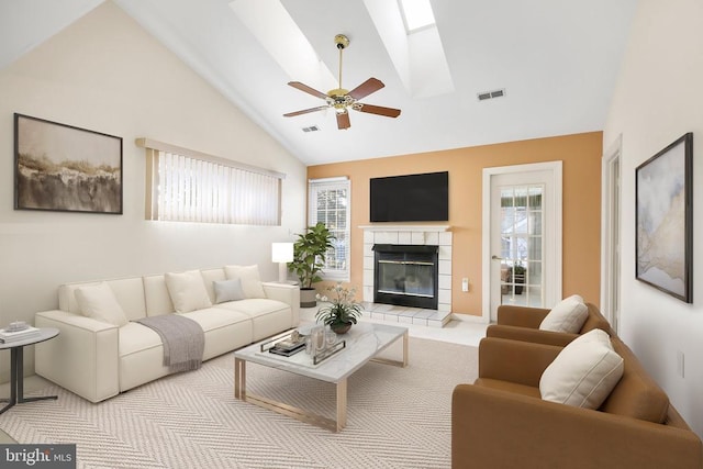 living room with ceiling fan, a fireplace, and vaulted ceiling with skylight