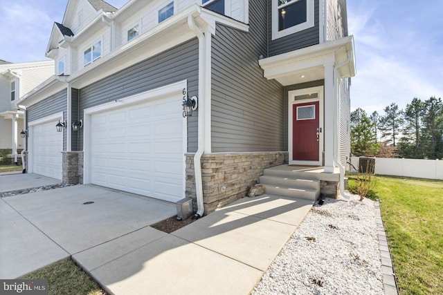 exterior space featuring stone siding, driveway, an attached garage, and fence