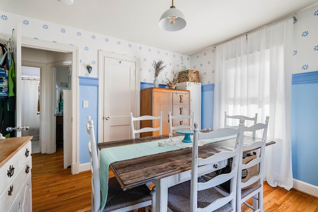 dining space featuring light wood finished floors, wallpapered walls, and baseboards