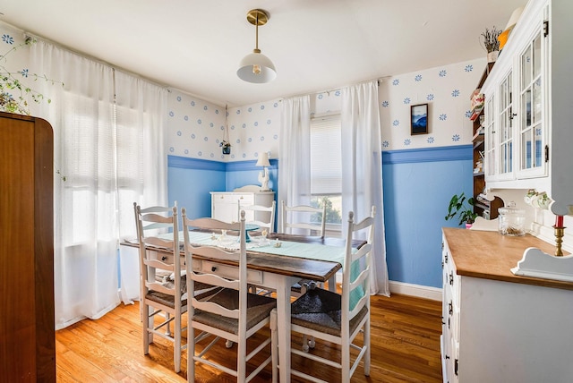 dining room with light wood-style floors, wainscoting, and wallpapered walls