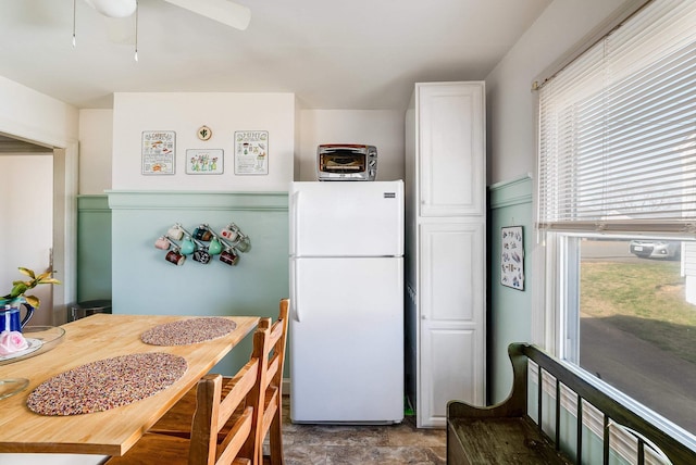 kitchen featuring stone finish floor, white cabinetry, and freestanding refrigerator