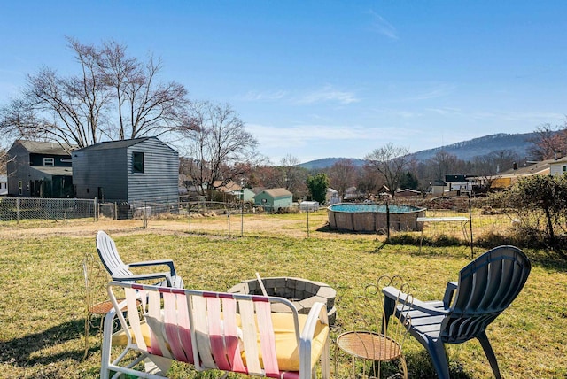 view of yard with an outdoor pool, a mountain view, an outdoor fire pit, and fence