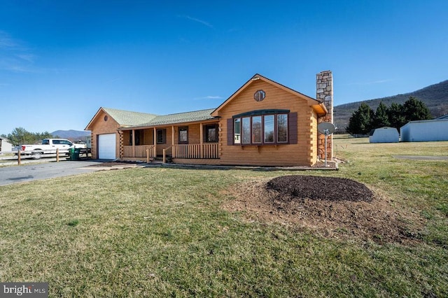 view of front of home featuring aphalt driveway, an attached garage, covered porch, a front lawn, and a chimney