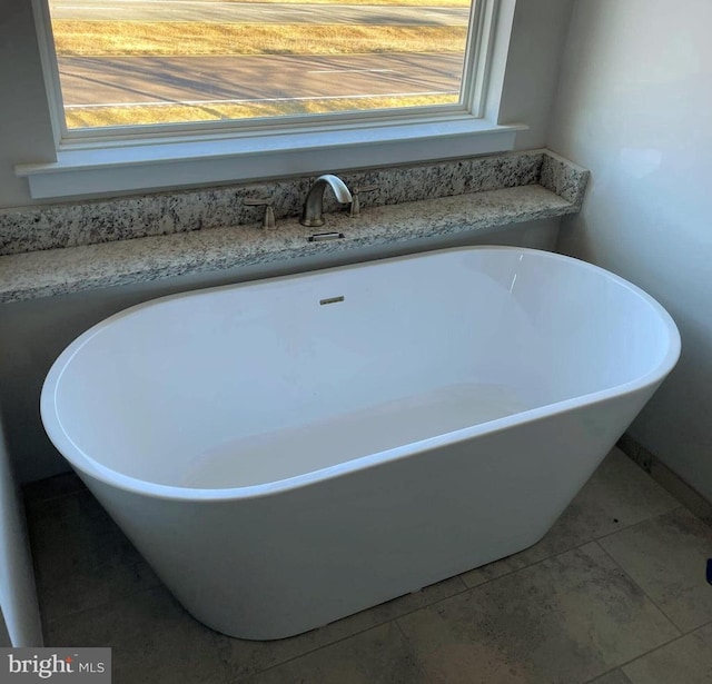 bathroom with a tub to relax in and a healthy amount of sunlight