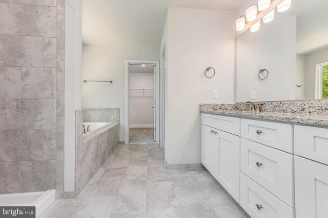 bathroom featuring a bath, a spacious closet, vanity, and baseboards