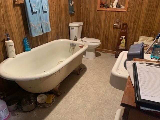 bathroom featuring toilet, wooden walls, and a tub to relax in