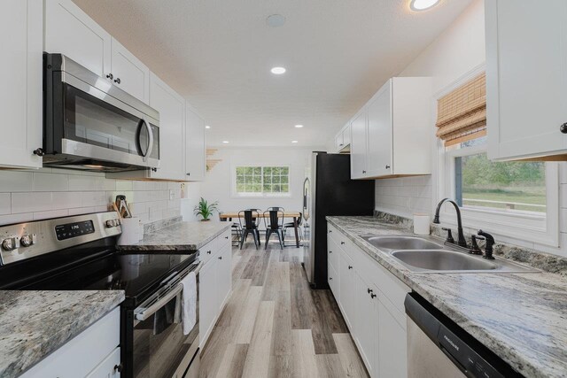 kitchen featuring light wood-style floors, white cabinetry, a sink, backsplash, and stainless steel appliances