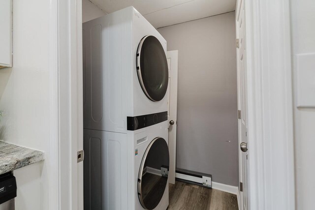clothes washing area featuring laundry area, stacked washer and dryer, dark wood-style flooring, baseboards, and baseboard heating