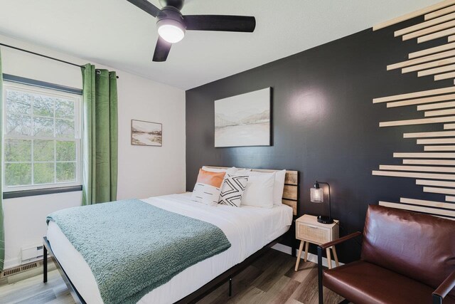 bedroom featuring a ceiling fan, wood finished floors, and an accent wall