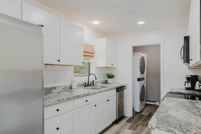 kitchen featuring stacked washer and dryer, wood finished floors, a sink, white cabinets, and stainless steel appliances