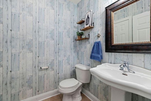 half bathroom featuring toilet, tile patterned floors, a sink, and baseboards