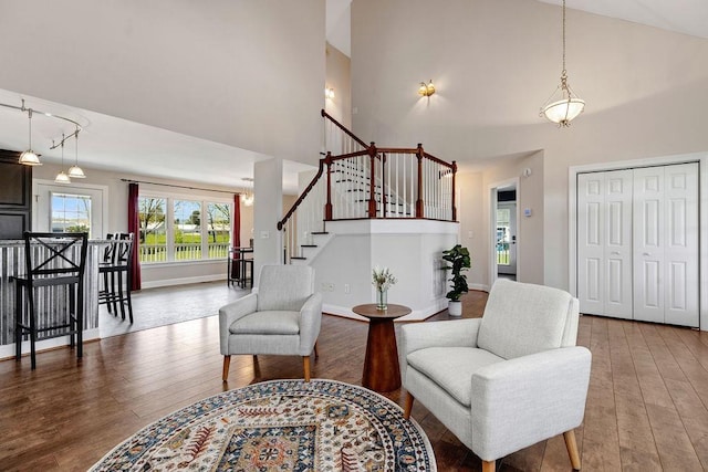 living area featuring high vaulted ceiling, baseboards, hardwood / wood-style flooring, and stairs
