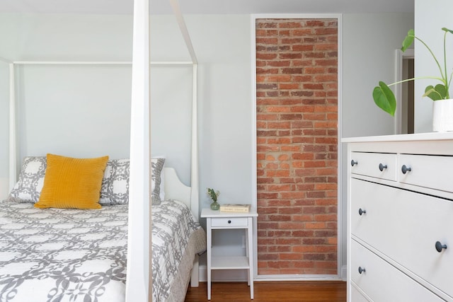 bedroom featuring baseboards, wood finished floors, and brick wall