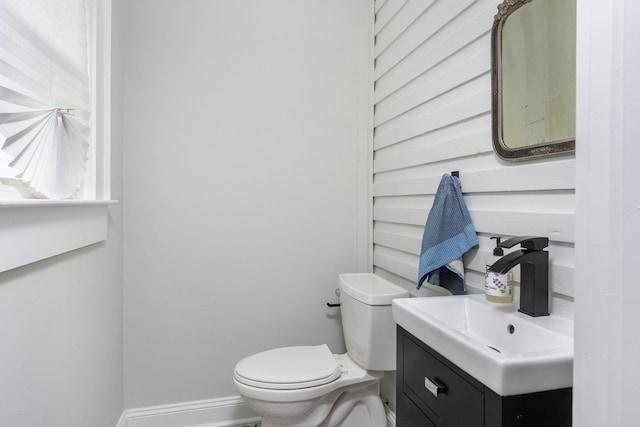 half bath featuring baseboards, toilet, and vanity