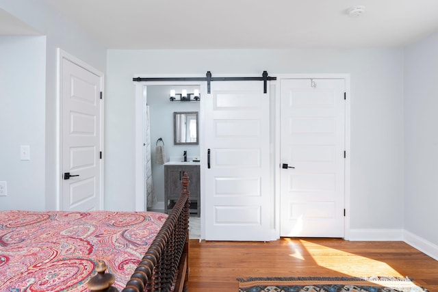 bedroom featuring baseboards, ensuite bathroom, a barn door, and wood finished floors