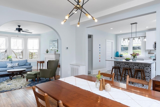 dining space with arched walkways, a healthy amount of sunlight, baseboards, and wood-type flooring