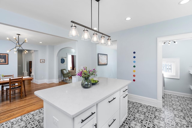 kitchen with arched walkways, white cabinets, a center island, and baseboards