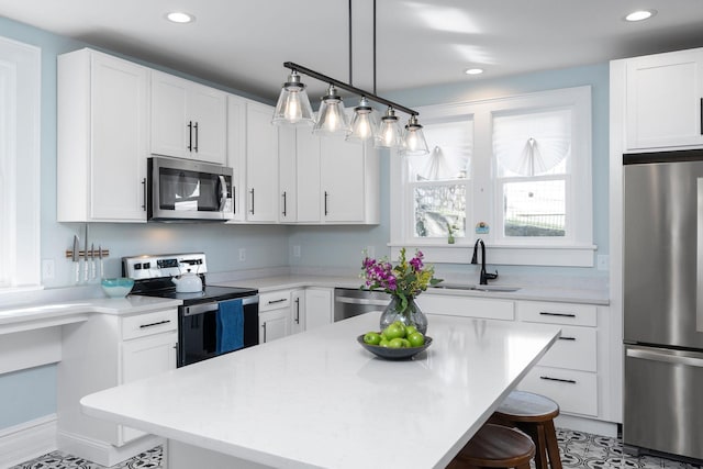 kitchen featuring a kitchen bar, a sink, stainless steel appliances, white cabinets, and light countertops