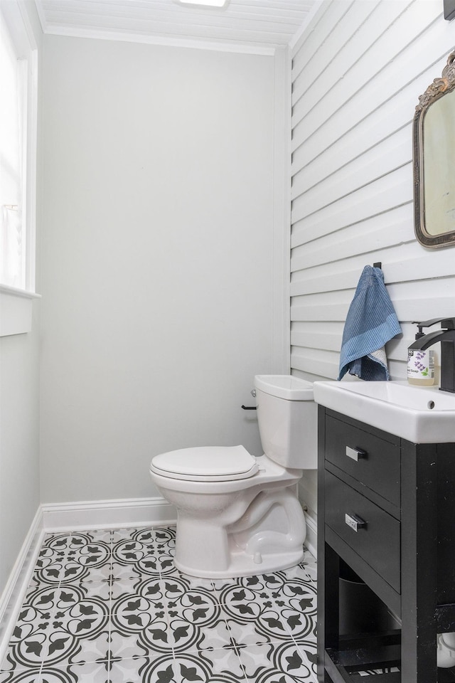 half bathroom with baseboards, a sink, crown molding, toilet, and tile patterned floors