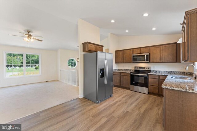 kitchen with vaulted ceiling, appliances with stainless steel finishes, sink, light stone counters, and light hardwood / wood-style floors