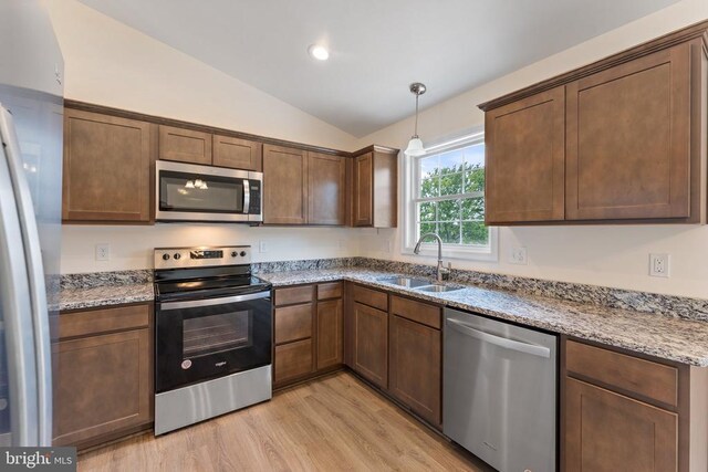 kitchen featuring sink, vaulted ceiling, light wood-type flooring, stainless steel appliances, and light stone countertops