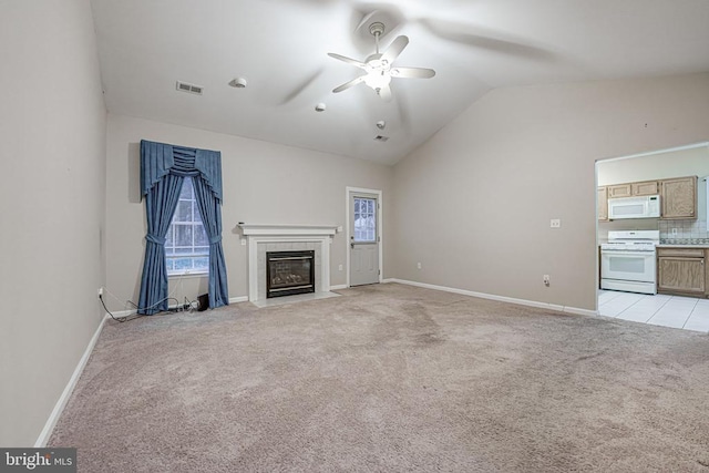 unfurnished living room featuring a tiled fireplace, lofted ceiling, light colored carpet, and ceiling fan