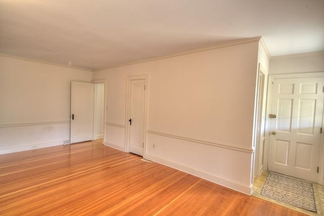 spare room featuring light wood finished floors, baseboards, and crown molding