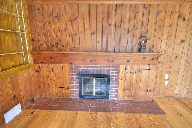 unfurnished living room with wood walls, a fireplace, visible vents, and wood finished floors