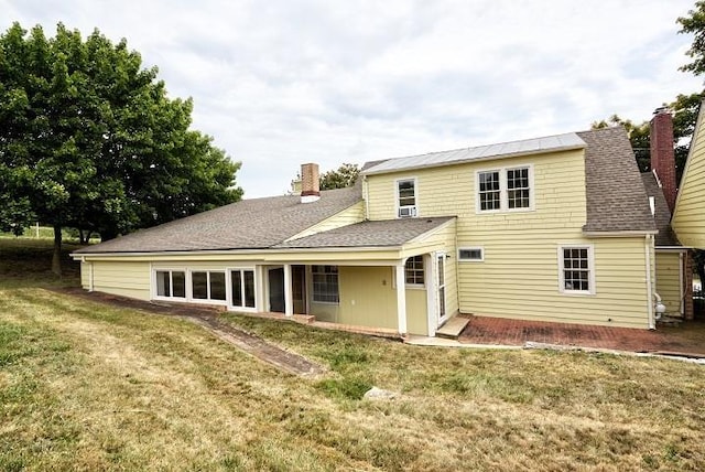 back of house with roof with shingles, a lawn, and a chimney