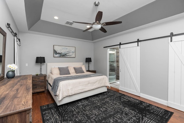 bedroom featuring ceiling fan, a barn door, dark hardwood / wood-style flooring, and a tray ceiling