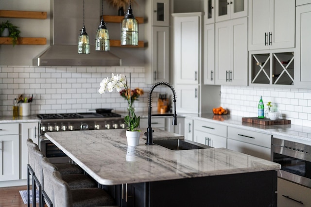 kitchen with sink, exhaust hood, light stone countertops, a kitchen island with sink, and white cabinets