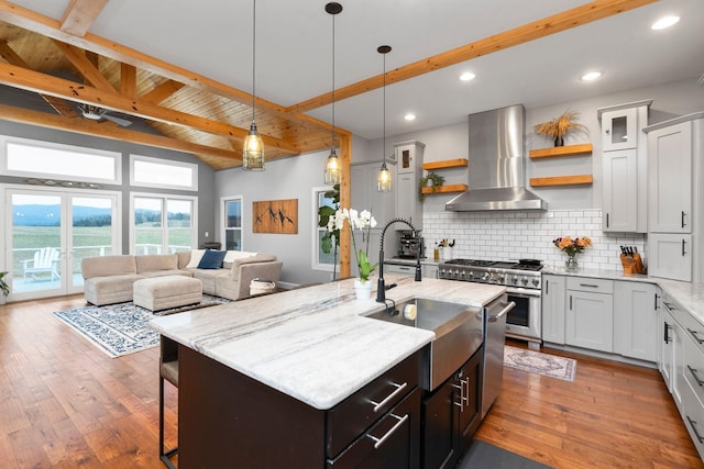 kitchen with light stone countertops, extractor fan, appliances with stainless steel finishes, and a kitchen island with sink