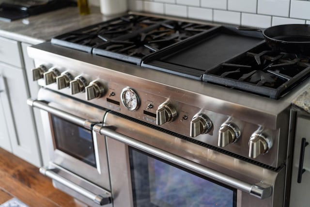 interior details featuring white cabinetry, dark stone countertops, tasteful backsplash, wood-type flooring, and range with two ovens