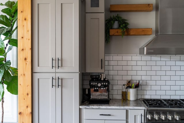 kitchen with wall chimney range hood, white cabinetry, backsplash, stone countertops, and stainless steel range with gas cooktop