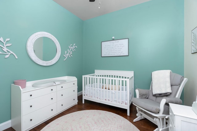 bedroom with ceiling fan, dark hardwood / wood-style floors, and a crib