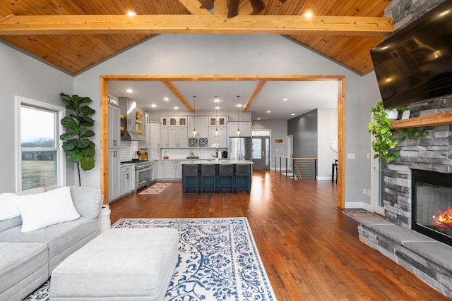 living room with beamed ceiling, a stone fireplace, plenty of natural light, and dark hardwood / wood-style flooring