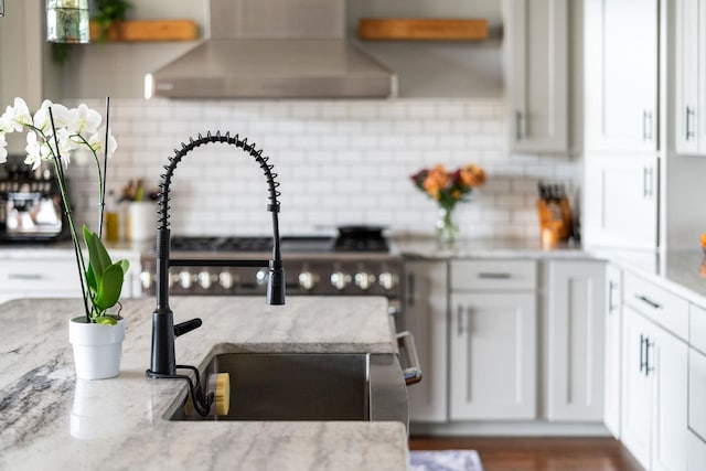 kitchen featuring white cabinetry, wall chimney exhaust hood, light stone countertops, and decorative backsplash